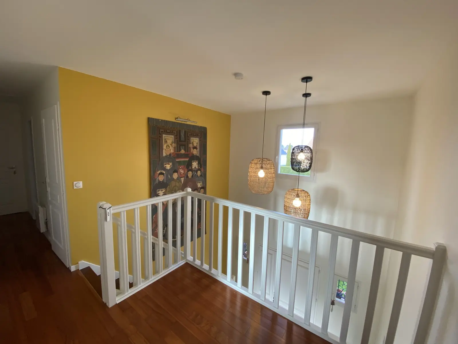 Photo d'un palier d'escalier. On distingue immédiatement les boiseries peintes en blanc immaculé, particulièrement la balustrade de l'escalier. La peinture est fraîche et uniforme, suggérant une rénovation soignée qui donne un aspect propre et moderne à l'ensemble.